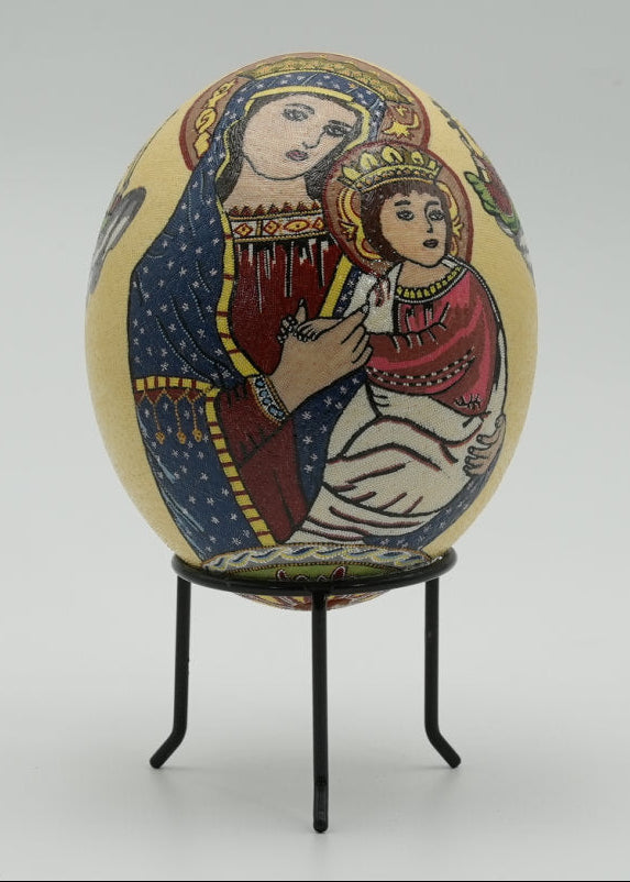 Intricately painted decorative egg featuring a religious scene of a woman holding a child, set against a softly lit background.