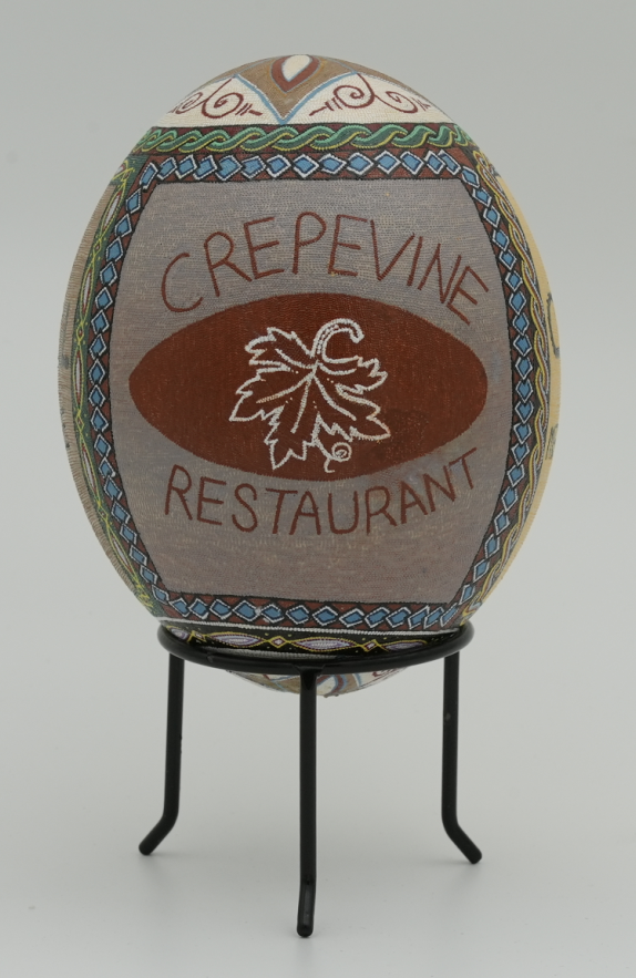 Decorative hand-painted egg featuring intricate designs and the text 'Crepevine Restaurant' on a smooth surface.