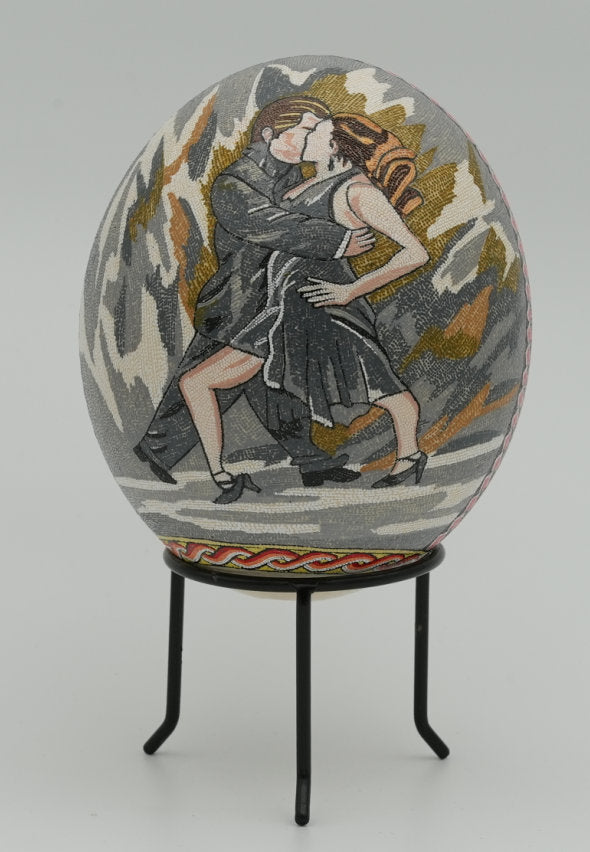 Intricately decorated decorative egg featuring a couple dancing, with vibrant colors and detailed embroidery on a textured surface.