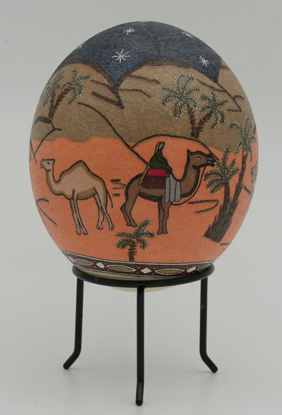 Decorative hand-painted egg featuring a desert scene with a camel and rider — intricate details on an earthy orange background