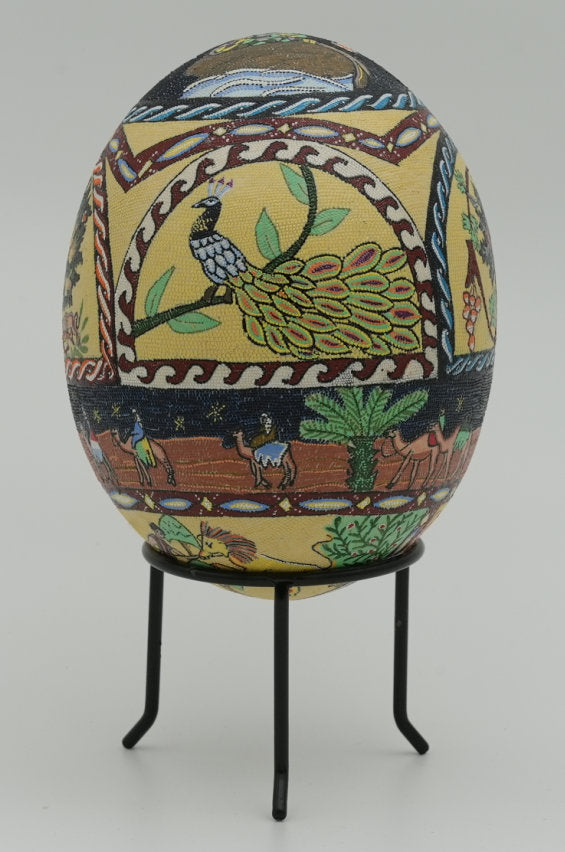 Intricately designed decorative egg featuring vibrant patterns and a peacock motif, displayed on a sleek black stand.