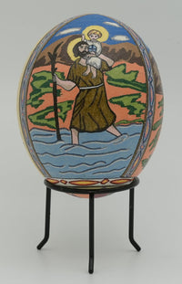Intricately decorated egg featuring a saint carrying a child across water, with vibrant colors and detailed imagery.