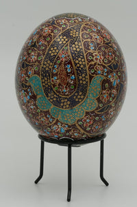 Intricately painted decorative egg resting on a black metal stand — featuring vibrant patterns in rich earth tones and turquoise accents.