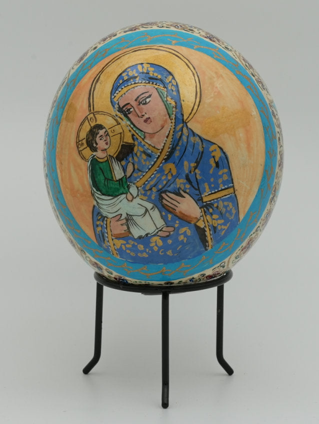 Intricately painted decorative egg featuring a blue-clad Virgin Mary holding baby Jesus, set against a soft grey background.