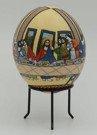 Intricately designed decorative egg featuring the Last Supper scene — vibrant colors on a textured surface with a stand.