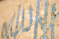 Intricate mosaic art featuring shimmering blue tiles on a textured beige background — a stunning decorative piece.