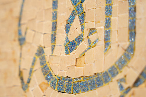 Intricate mosaic tile art featuring shimmering blue and gold accents set against a warm beige background, showcasing detailed craftsmanship.