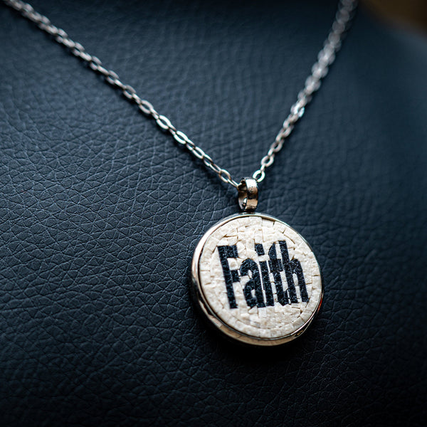 Stylish silver necklace featuring a round pendant with the word 'Faith' intricately engraved on a textured surface.