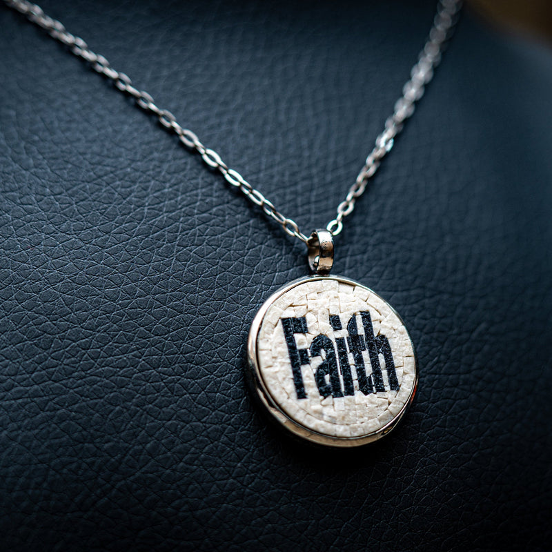 Stylish silver necklace featuring a round pendant with the word 'Faith' intricately engraved on a textured surface.