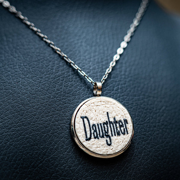 Silver pendant necklace featuring a textured cream background with the word 'Daughter' elegantly inscribed in black.