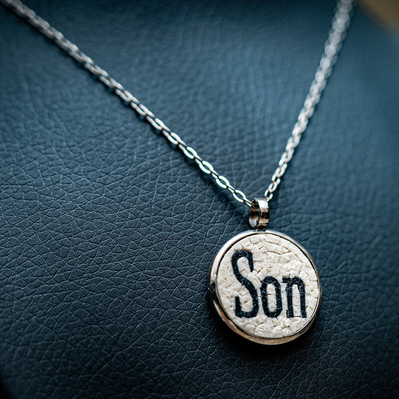 Silver pendant necklace featuring a textured charm with the word 'Son' — a meaningful accessory on a delicate chain