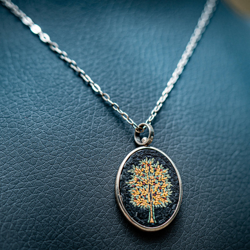 Intricate pendant necklace featuring a vibrant tree design on a dark background — silver chain with a polished finish