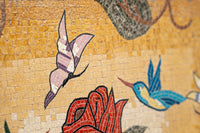Vivid mosaic art featuring colorful hummingbirds and roses on a textured golden background — intricate tile work with delicate details.