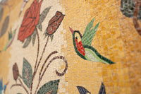 Vibrant mosaic artwork featuring a colorful hummingbird among floral designs — intricate tile patterns create a lively scene.