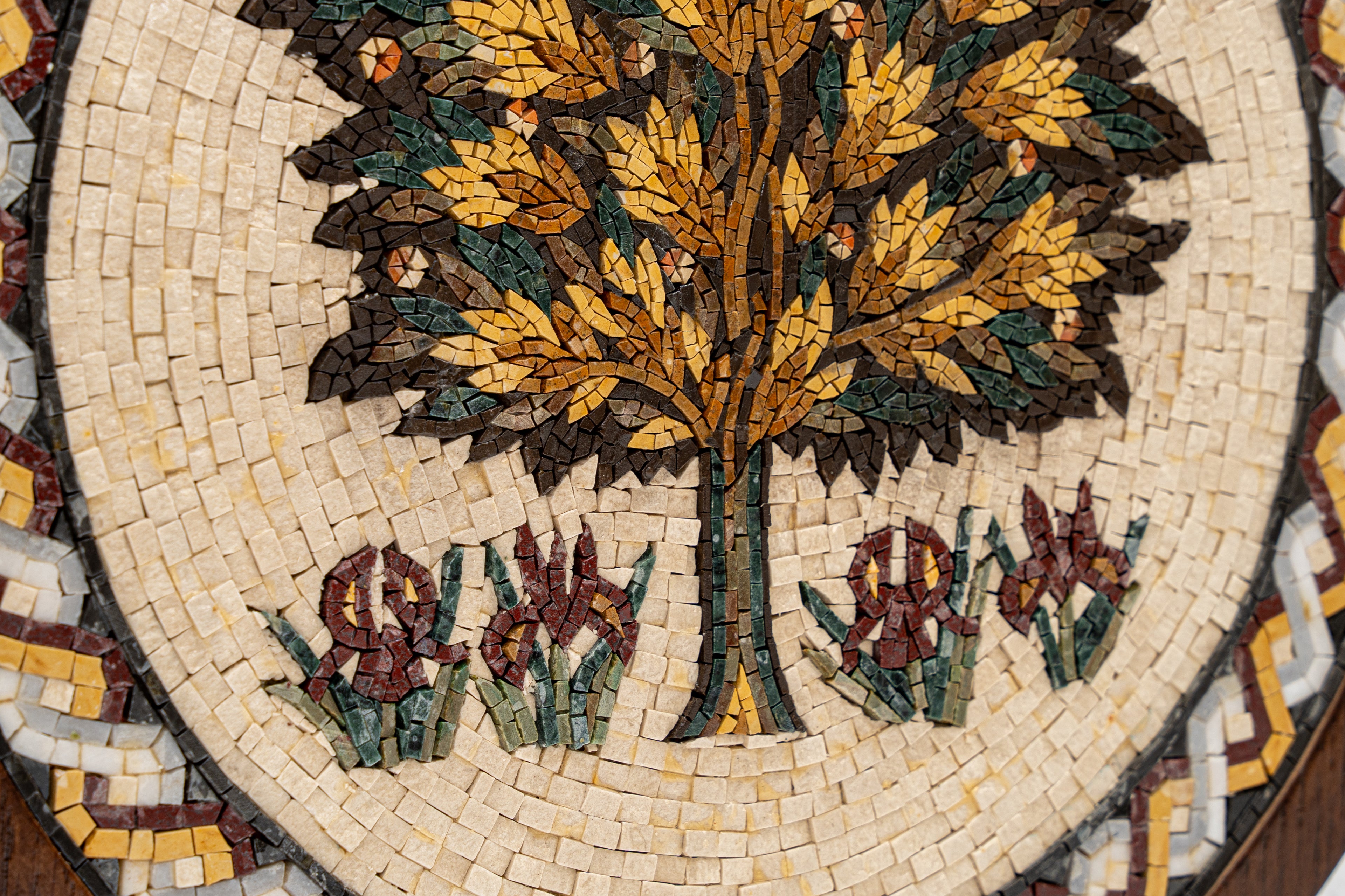 Intricate mosaic artwork featuring a golden tree surrounded by blooming irises — crafted with colorful stone tiles for texture.