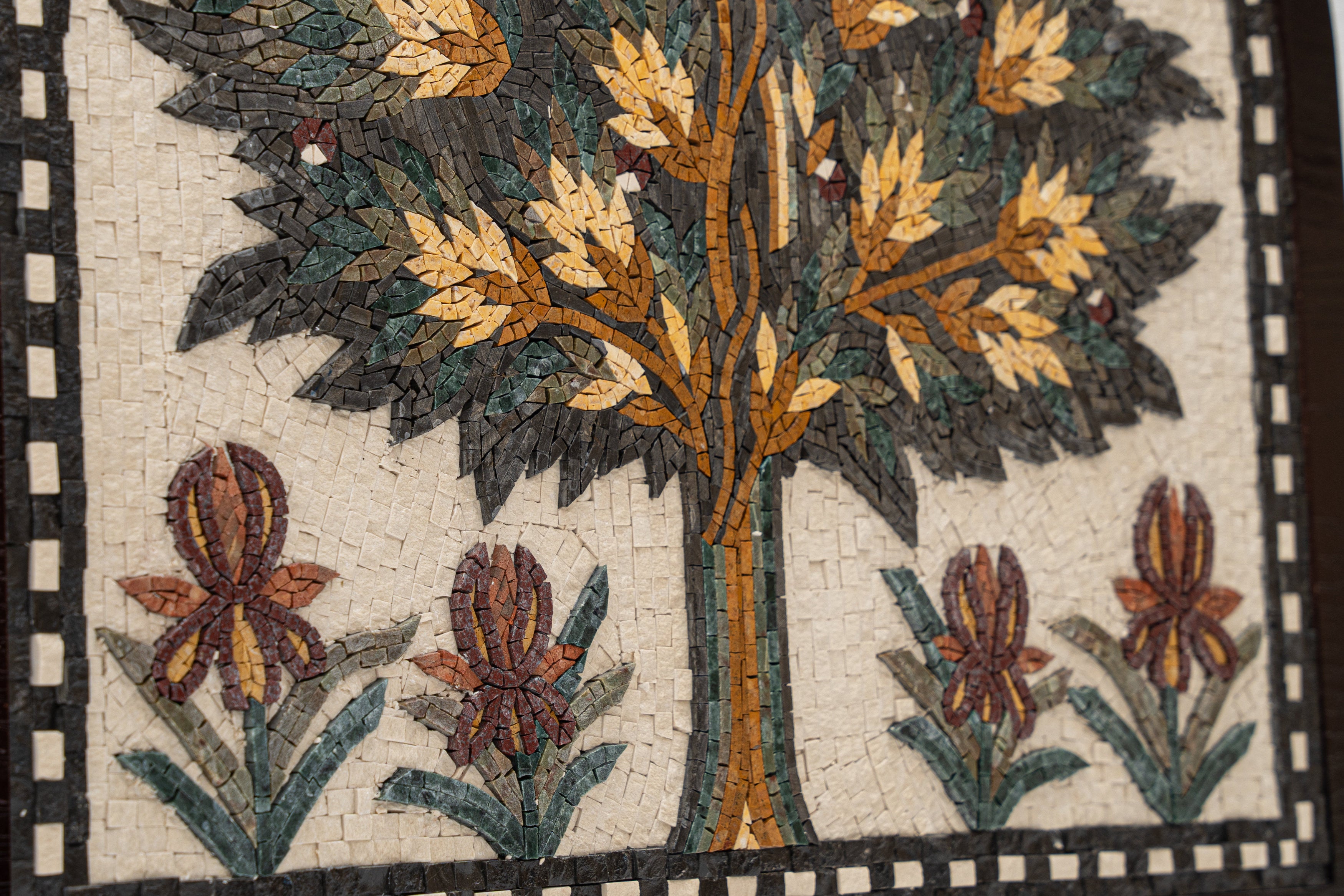 Intricate mosaic artwork featuring a vibrant tree design with golden leaves and colorful floral accents on a textured background