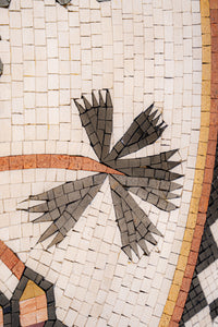 Intricate mosaic tile design featuring dark grey and light beige pieces arranged in a floral pattern with textured surfaces.