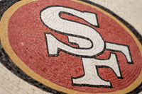 Colorful mosaic featuring the SF logo on a textured surface — intricate design with vibrant red and black accents
