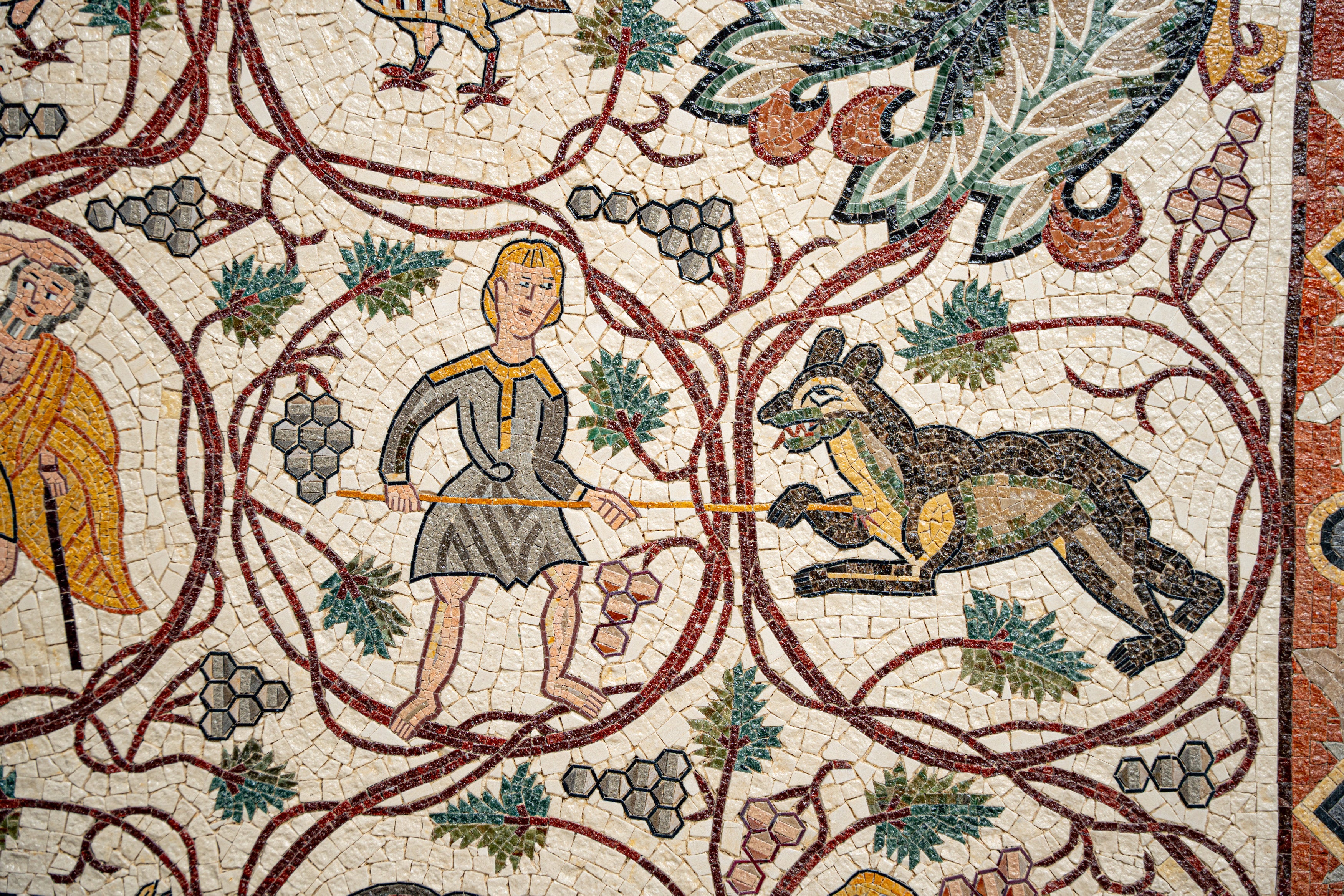 Intricate mosaic artwork depicting a boy wielding a stick beside a wild animal among grapevines — showcasing ancient craftsmanship.