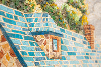 Intricate mosaic artwork featuring a textured blue roof with vibrant green foliage in the background — a colorful and detailed composition.