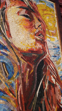 Vibrant mosaic art featuring a woman's face with flowing hair — intricate tiles in warm hues and cool blues create depth.