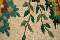 Intricate mosaic design featuring green leaves and colorful flowers against a textured beige background — showcasing artisanal craftsmanship.