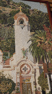 Intricate mosaic artwork depicting a church facade with vibrant greenery and a palm tree — detailed craftsmanship in stone tiles.