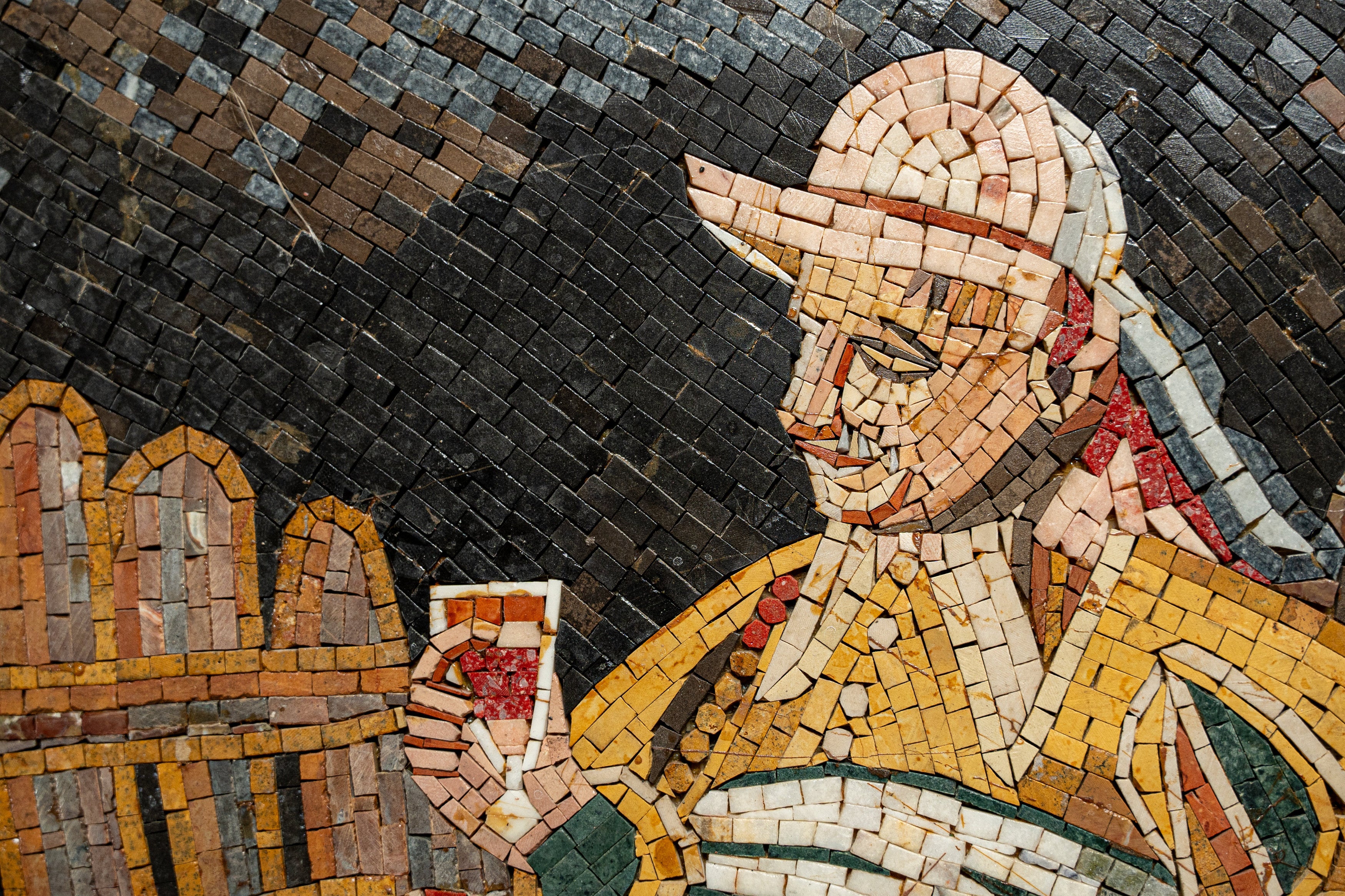 Intricate mosaic art depicting a man holding a drink, featuring vibrant ceramic tiles in earthy tones.