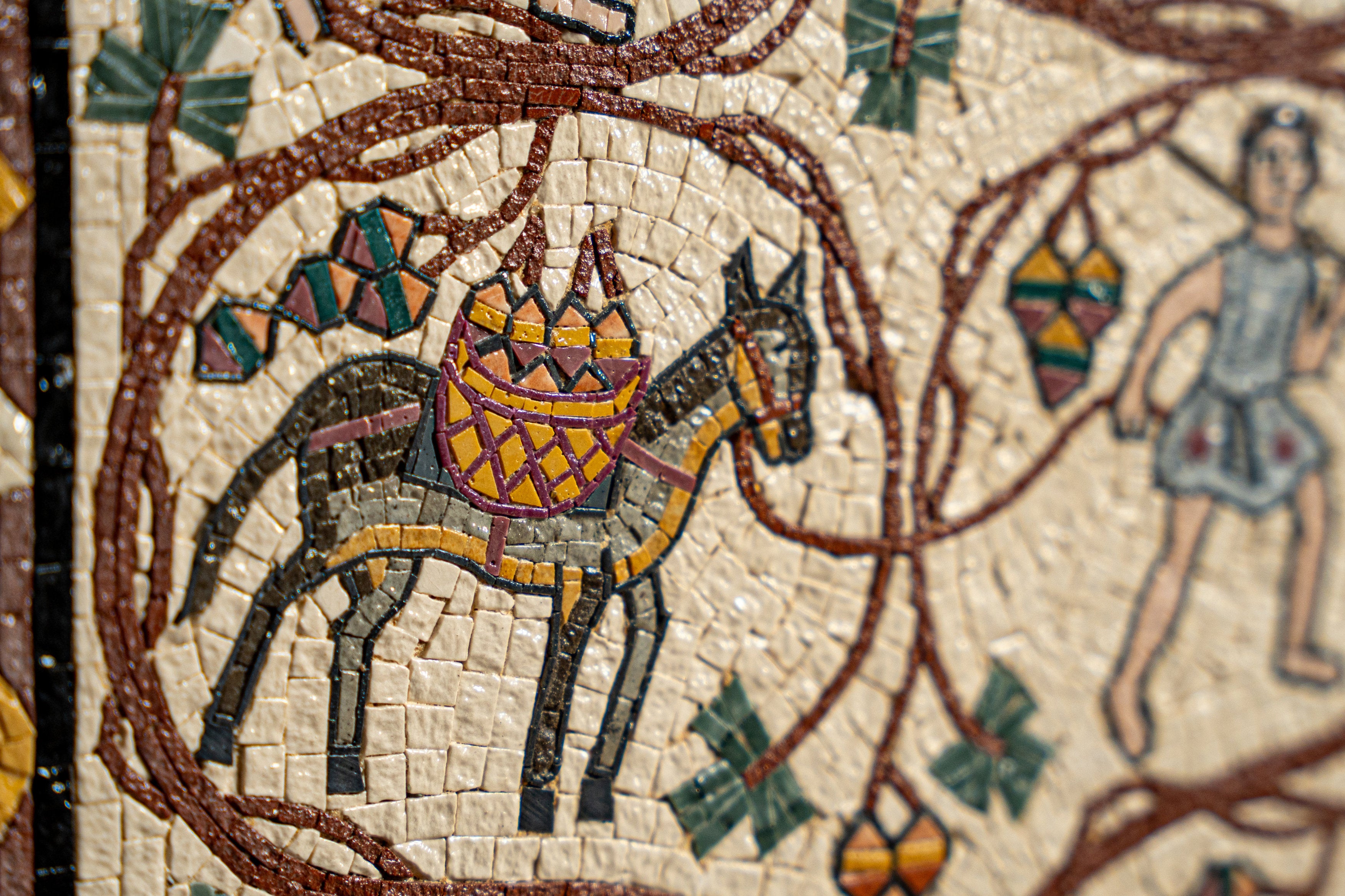 Intricate mosaic art featuring a black horse adorned with a colorful basket, surrounded by detailed vines and figures.