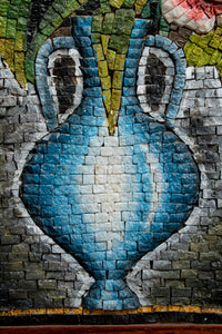 Intricate mosaic vase design in blue and white, showcasing textured tiles against a vibrant background of green and grey.