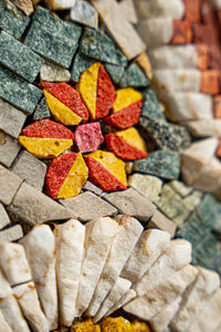 Intricate mosaic art featuring a vibrant flower design in red, yellow, and orange surrounded by textured stone tiles