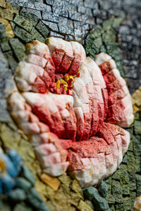 Intricate mosaic flower design featuring vibrant red and white tiles set against a textured stone background