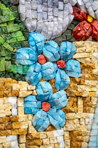 Vibrant mosaic art featuring blue flowers with red centers against a textured stone background — intricate craftsmanship in colorful tiles.