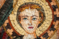 Intricate mosaic artwork featuring a serene face with striking blue eyes and a radiant golden halo made of natural stone tiles.