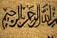 Intricate mosaic wall art featuring black calligraphy on textured golden tiles — a striking blend of culture and craftsmanship.