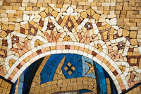 Intricate mosaic art featuring a crown design in earthy tones and vibrant blue tiles — a stunning display of craftsmanship.