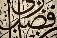 Intricate mosaic art featuring Arabic calligraphy in earthy tones — a blend of dark and light tiles creating texture.