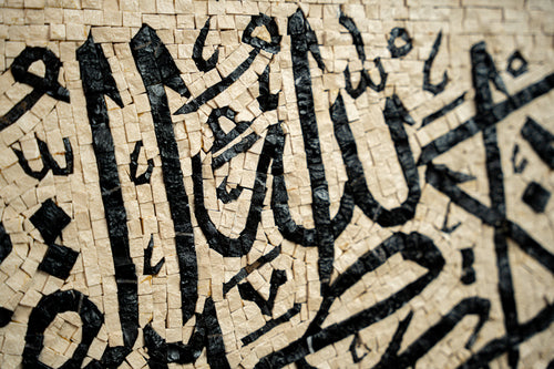 Intricate mosaic art featuring Arabic calligraphy in bold black on a textured beige background — a stunning cultural expression.