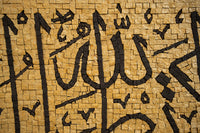 Intricate calligraphy art piece on textured golden tiles — showcasing detailed black lettering against a warm backdrop