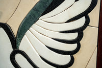 Intricate mosaic wing design featuring polished white and black stones with a touch of green for a striking contrast