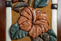 Intricate carved floral wall art featuring a vibrant orange hibiscus and detailed green leaves on a textured background