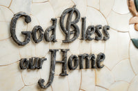 Intricately carved wall plaque featuring the phrase 'God Bless our Home' in dark stone against a textured cream background.
