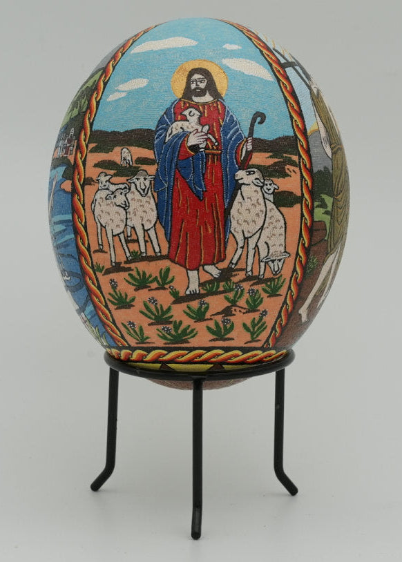 Intricately decorated Easter egg featuring a shepherd in vibrant red robes surrounded by sheep against a pastoral backdrop.