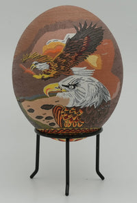 Intricately designed decorative egg featuring detailed eagle illustrations in earthy tones — a unique artistic piece on a black stand.