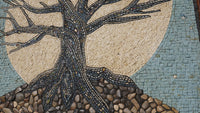 Intricate mosaic tree design featuring textured stones and tiles against a pale blue background — a captivating artistic representation.