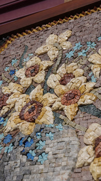 Intricate mosaic art featuring sunflowers and blue flowers made from natural stone tiles with a textured finish