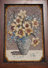Intricate mosaic artwork featuring a vase of yellow flowers with blue accents — crafted from natural stone tiles.