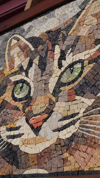 Intricate mosaic cat artwork featuring vibrant green eyes and textured stone tiles in earthy tones that create depth.